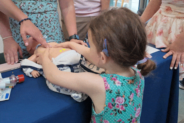 Little girl giving CPR to manikin baby.