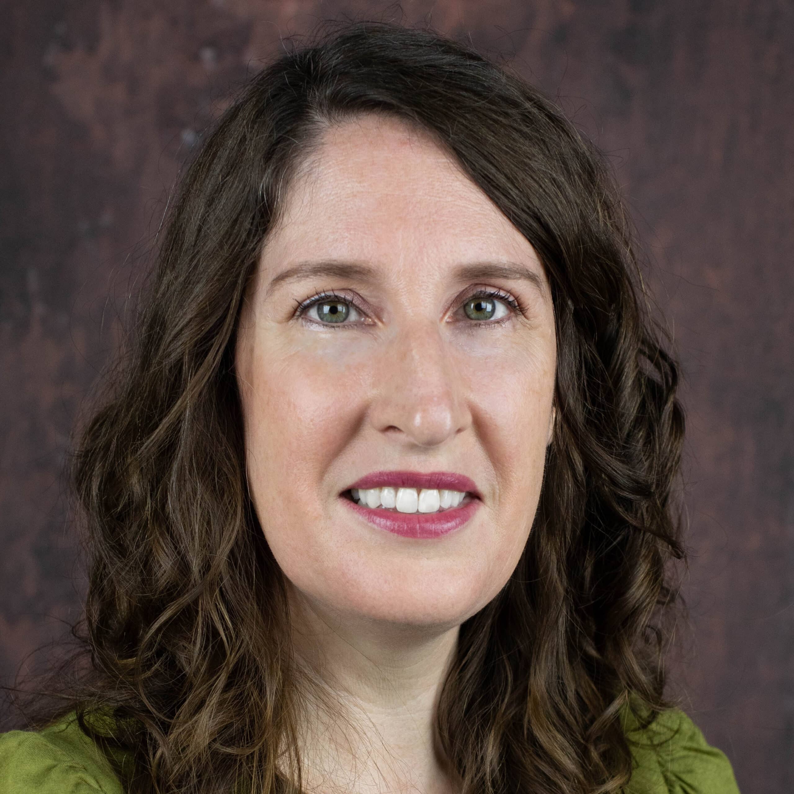Bridget Fletcher smiles for a headshot in front of a brown background wearing a green blouse.