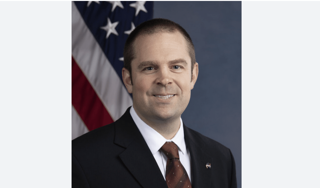 NASA official dressed in suit standing in front of American flag