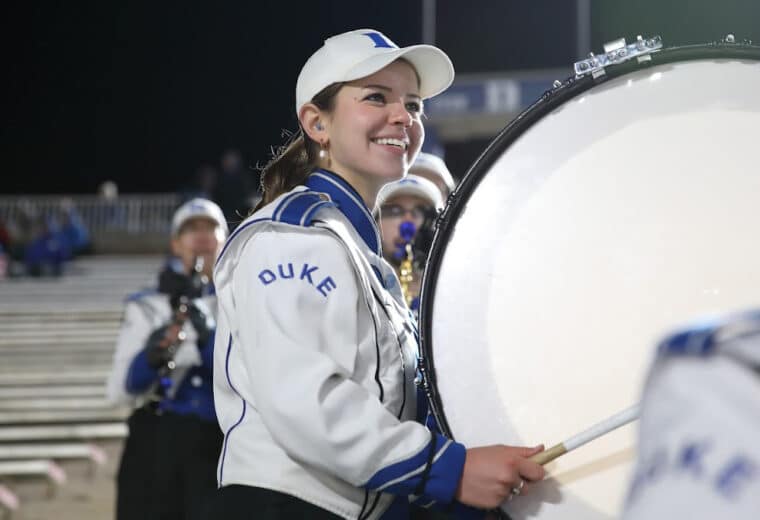 Duke marching band member Sarah Willmann plays bass drum at night stadium.
