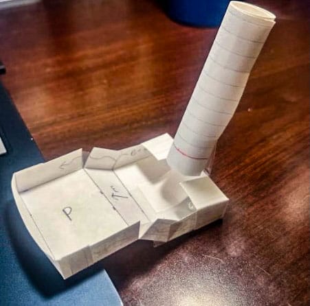 A paper cutout that is a tube on the top and an open box on the bottom.