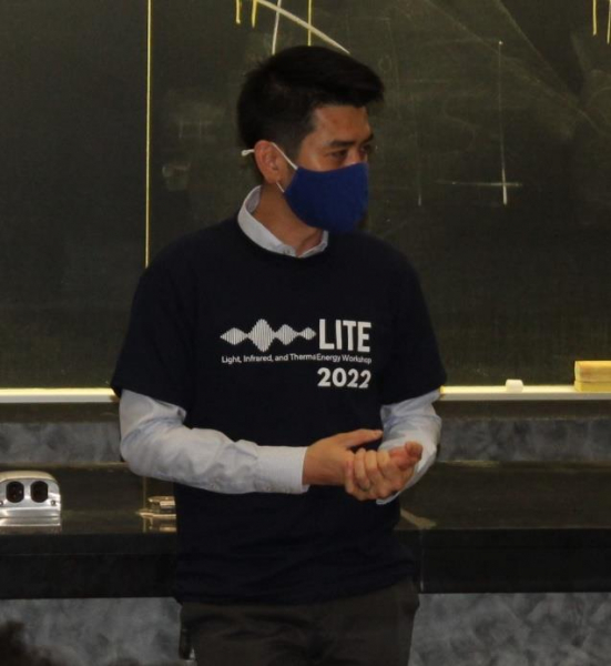 Man with black hair wearing blue mask and blue shirt with blackboard in background