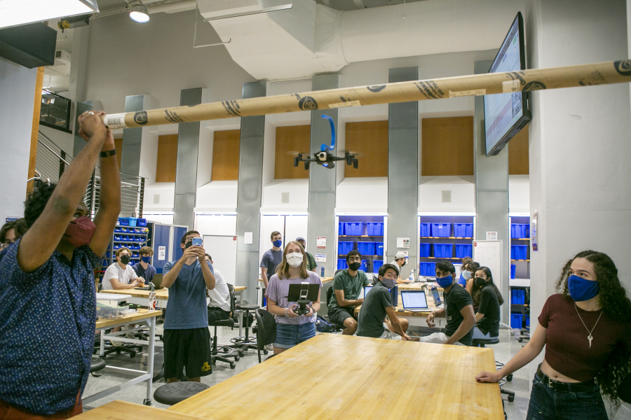 Students hold a bar overhead, where a drone waits to drop a trap using a hook